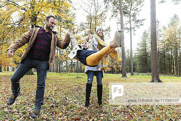 Smiling girl swinging while holding hands of parents standing in forest