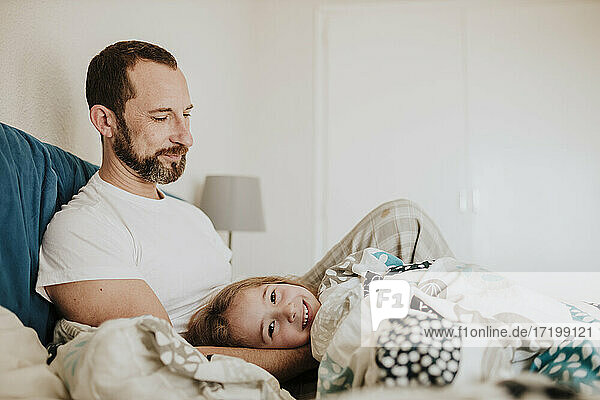 Smiling daughter lying on father's lap on bed at home