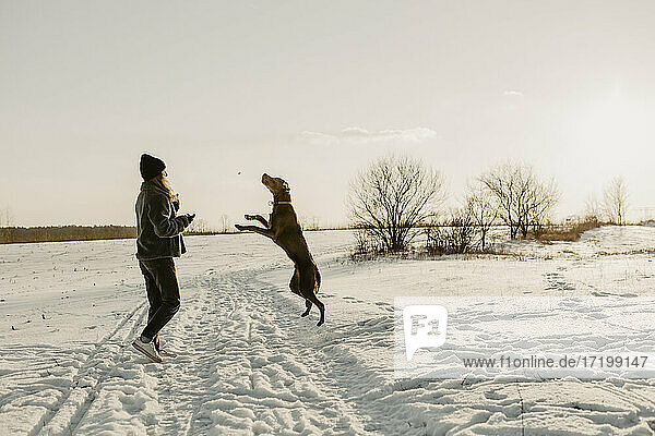 Teenager-Mädchen spielt mit Hund im Schnee bei Wintersonnenaufgang