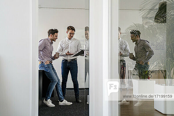 Männliche Unternehmer  die über ein Klemmbrett diskutieren  gesehen durch eine Tür im Büro