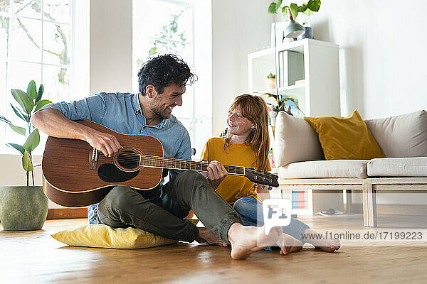 Father playing guitar while sitting by daughter at home