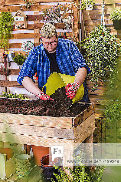 Junger Mann bereitet das Substrat für einen städtischen Garten aus Paletten auf seiner Terrasse vor