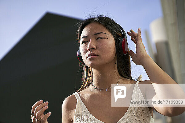 Asiatische Frau schaut weg  während sie an einem sonnigen Tag über Kopfhörer Musik hört