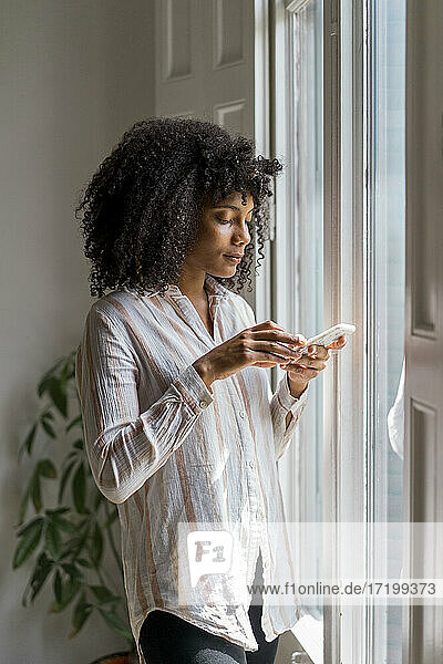 Schöne Unternehmerin  die ein Smartphone benutzt  während sie in der Nähe des Fensters im Büro steht