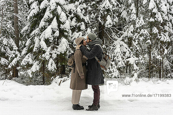Junges Paar mit Rucksack  das sich küsst  während es im Wald steht