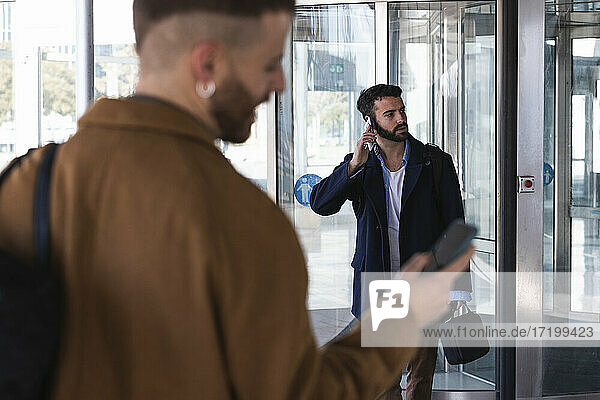 Businessman talking on mobile phone while standing with coworker in background against building