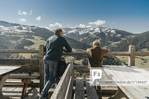 Vater mit zwei Kindern  die sich an ein Geländer lehnen  mit Blick auf die Leoganger Berge  Salzburger Land  Österreich