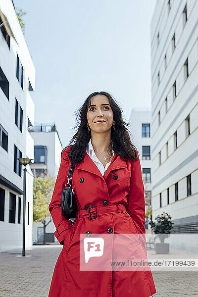 Lächelnde Unternehmerin mit den Händen in den Taschen  die wegschaut  während sie auf dem Fußweg geht