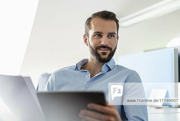 Businessman with paper and digital tablet smiling at office