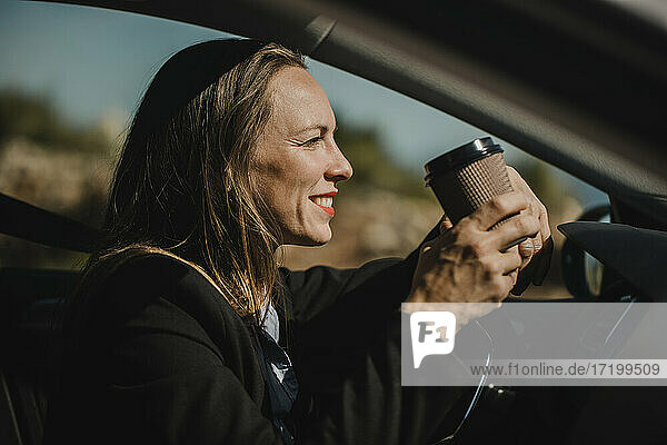 Unternehmer  der an einem sonnigen Tag im Auto sitzt und Kaffee trinkt