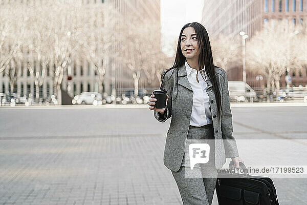 Nachdenkliche reife Geschäftsfrau mit Tasche  die eine Kaffeetasse hält  während sie in der Stadt wegschaut