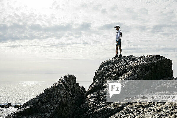Man standing on rock formation against cloudy sky