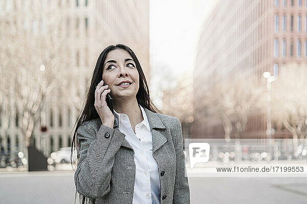 Reife Geschäftsfrau  die mit ihrem Smartphone spricht und dabei seitwärts in die Stadt schaut