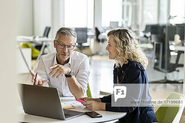 Älterer Geschäftsmann mit Laptop  der einem Kollegen einen Geschäftsplan erläutert  während er am Tisch im Büro sitzt