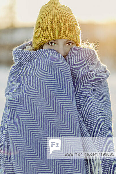 Portrait of beautiful girl wearing knit hat warming herself up with wool blanket