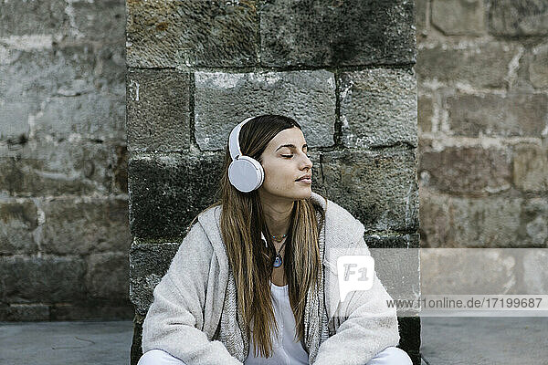 Junge Frau hört Musik über Kopfhörer an einer Steinmauer