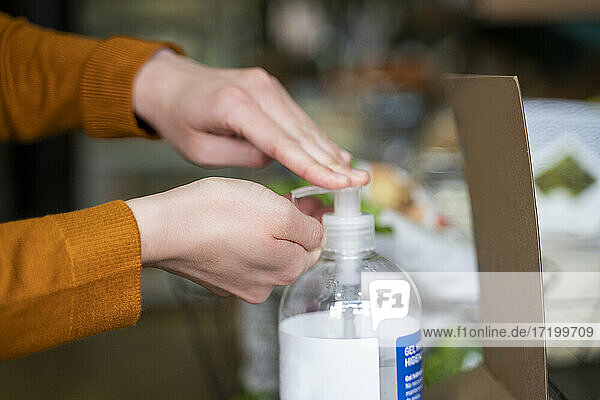 Woman disinfecting hands using sanitizer at store