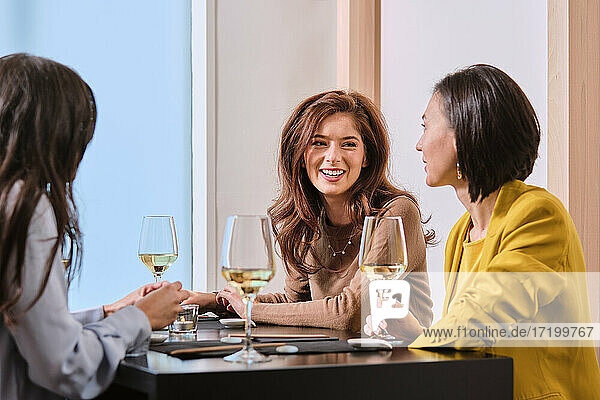 Young female friends with wine glasses while sitting at table in restaurant