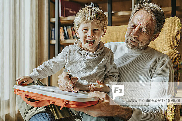Father teaching drawing to cheerful son while sitting on chair