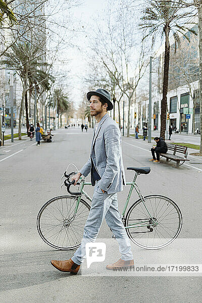 Männlicher Berufstätiger mit Hut beim Spaziergang mit dem Fahrrad in der Stadt