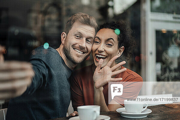 Smiling couple looking at video call on mobile phone while sitting at cafe