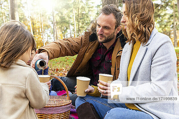 Vater gießt Kaffee in die Tasse seiner Tochter  während er mit seiner Familie im Wald sitzt
