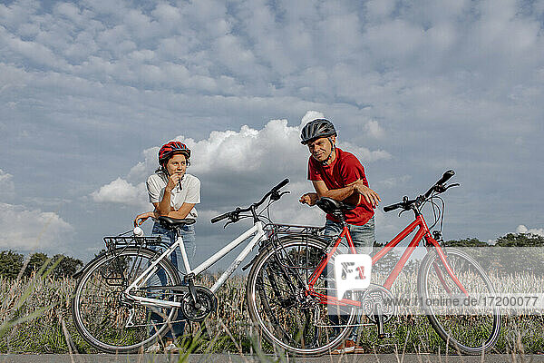 Daughter with father leaning on bicycle while standing at agricultural field against cloudy sky