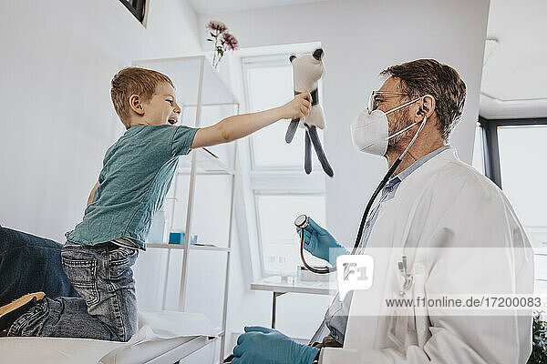 Allgemeinmediziner  der einen verspielten Jungen untersucht  der mit einem Spielzeug im Untersuchungsraum spielt