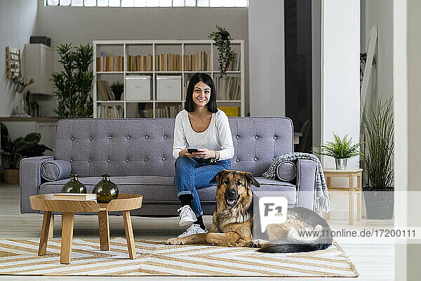 Lächelnde junge Frau mit Haushund im Wohnzimmer
