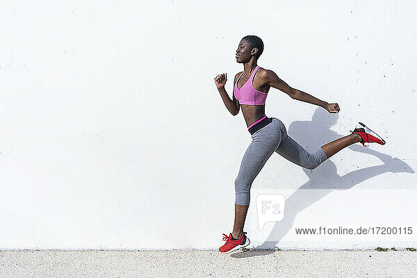 Young female athlete running against white wall during sunny day