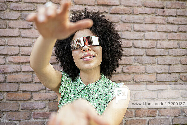Junge Afro-Frau mit futuristischer Sonnenbrille vor einer Backsteinmauer