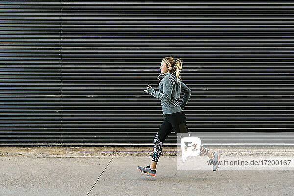 Female athlete running on sidewalk by wall during sports training