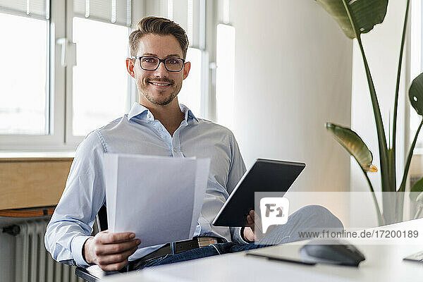 Confident businessman with document and digital tablet at office