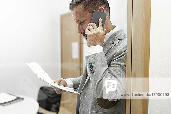 Geschäftsmann mit Dokumenten im Gespräch über Smartphone im Büro