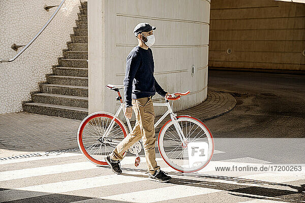 Mann mit Fahrrad schaut beim Überqueren der Straße an der Mauer weg  während der Pandemie