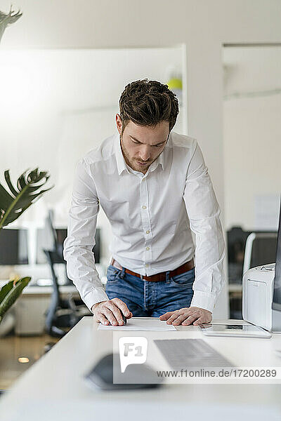 Male entrepreneur analyzing document at desk in office