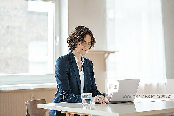 Reife Geschäftsfrau mit Laptop auf dem Tisch im Büro zu Hause