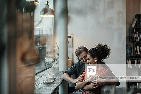 Lächelnde Frau lehnt sich an einen Mann  während sie im Café sitzt