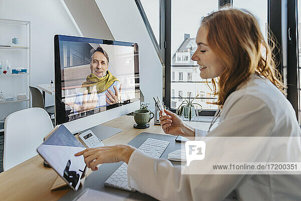 Lächelnder Patient im Gespräch mit dem Arzt über den Computer  während er im Büro sitzt