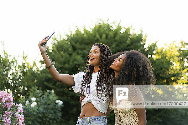 Fashionable female friends taking selfie by tree during summer