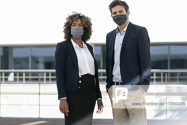 Berufstätige mit Gesichtsschutzmaske  die auf die Terrasse eines Bürogebäudes starren
