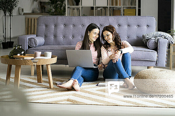 Junge Frau mit Laptop  die ihre Mutter anlächelt  während sie im Wohnzimmer sitzt