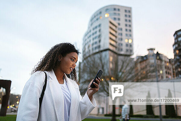 Junge Frau benutzt Smartphone im Park bei Sonnenuntergang