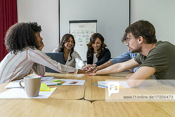 Multi-ethnische männliche und weibliche Kollegen stapeln ihre Hände im Sitzungssaal im Büro