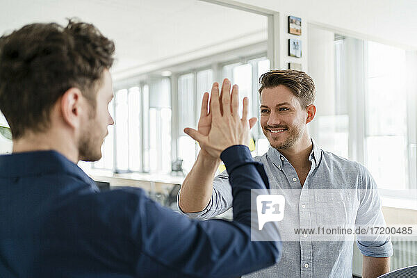 Smiling business man doing high-five with male colleague in office