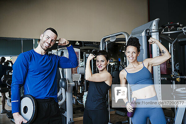 Smiling sports people flexing muscles while standing in health club