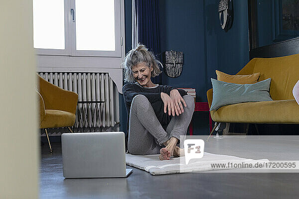 Smiling senior woman watching tutorial on laptop while sitting at home