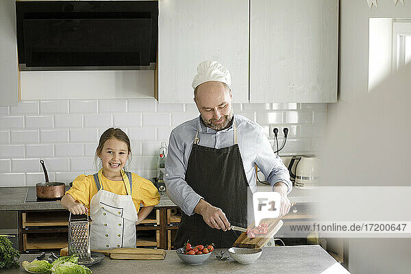 Lächelnde Tochter steht neben ihrem Vater  der in der Küche zu Hause Essen zubereitet