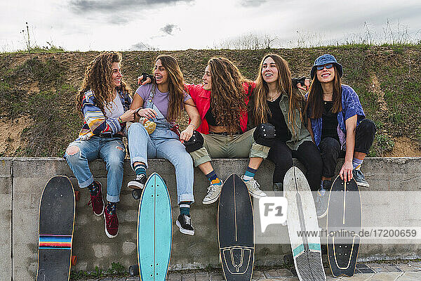 Fröhliche Freundinnen haben Spaß  während sie auf einer Stützmauer sitzen