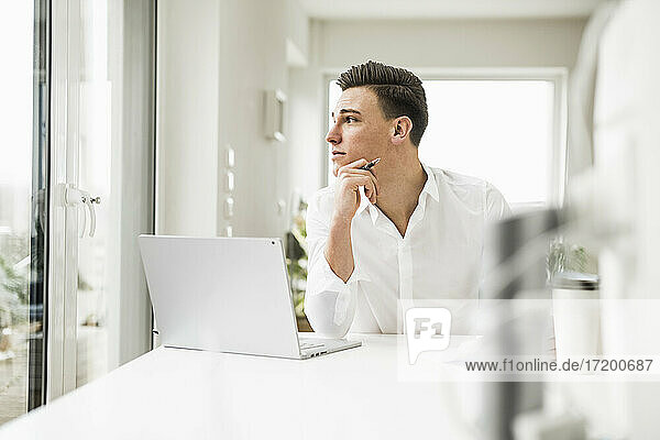 Junger männlicher Berufstätiger  der durch das Fenster schaut  während er in seinem Büro zu Hause sitzt